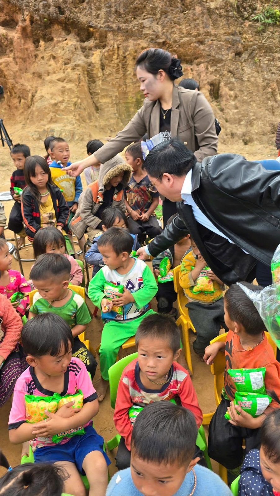 Trẻ em vùng cao ngồi nhận bánh kẹo từ đoàn thiện nguyện CEO1987 dưới chân núi đá trong ngày khởi công