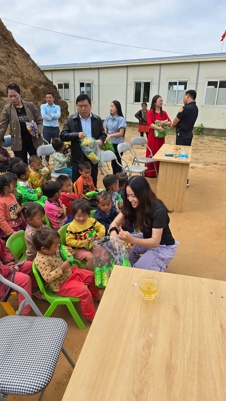 Các em nhỏ quây quần nhận quà bên công trình Trường Mầm Non Thắp Sáng Tương Lai đang xây dựng dở dang
